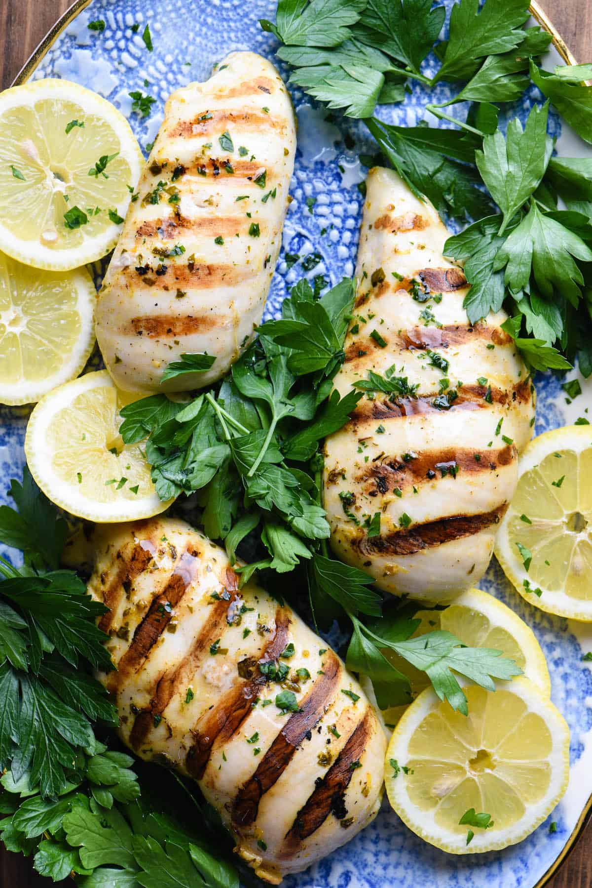 This Greek Chicken Marinade is a simple, fast recipe that results in juicy, succulent chicken every single time! | foxeslovelemons.com Cooked chicken pieces on pretty blue platter with herbs and lemons slices.