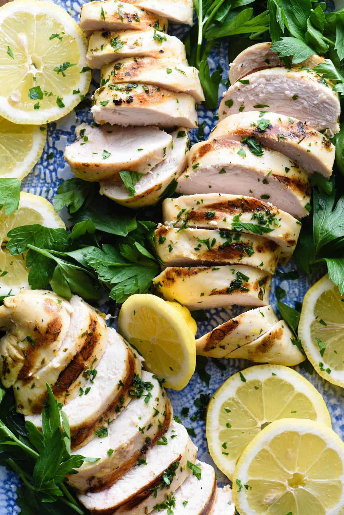 This Greek Chicken Marinade is a simple, fast recipe that results in juicy, succulent chicken every single time! | foxeslovelemons.com Sliced grilled chicken breasts with lemon slices and parsley.