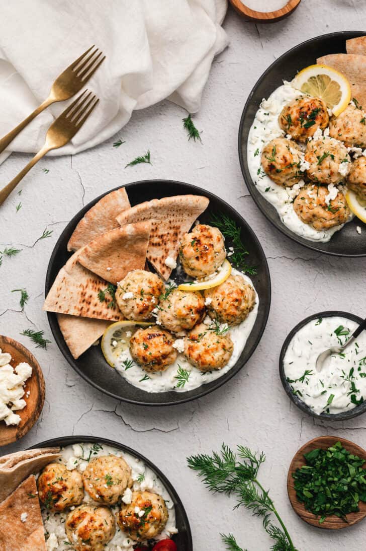 Mediterranean chicken meatballs in black bowls with yogurt sauce, pita bread and lemon slices.