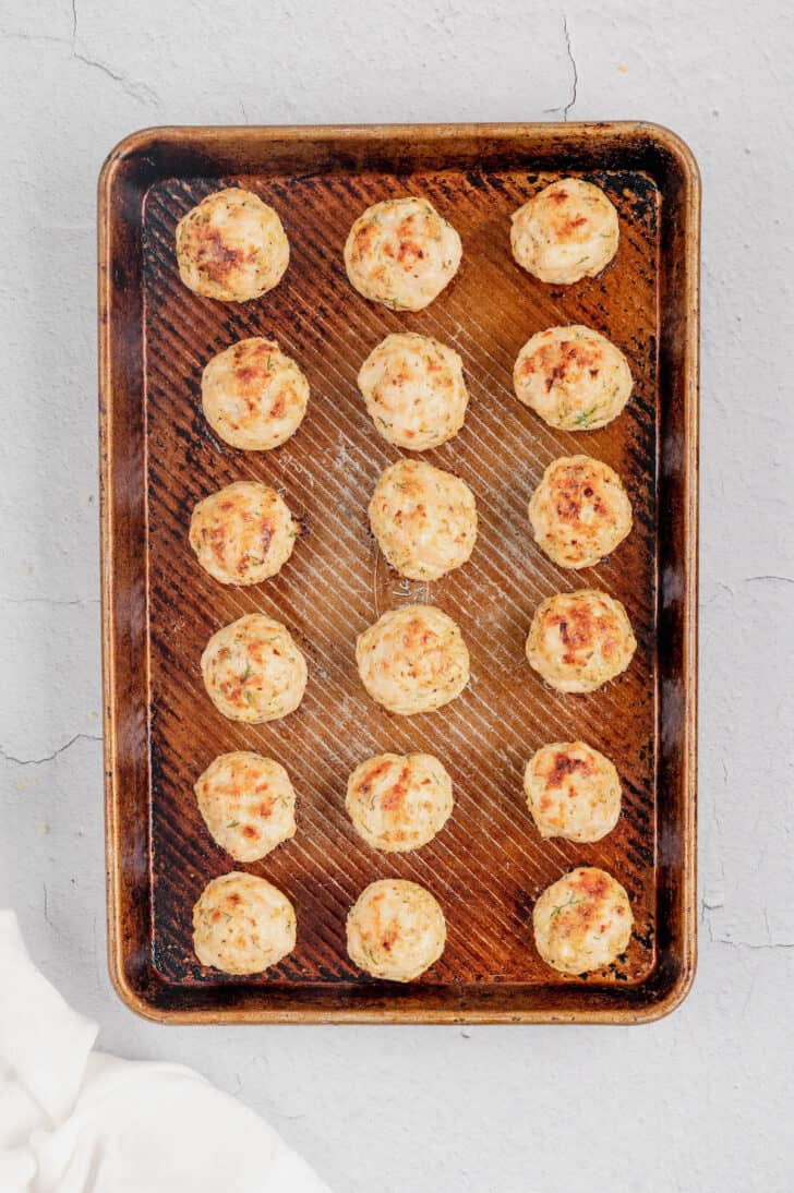 Greek chicken meatballs on a rimmed baking pan.