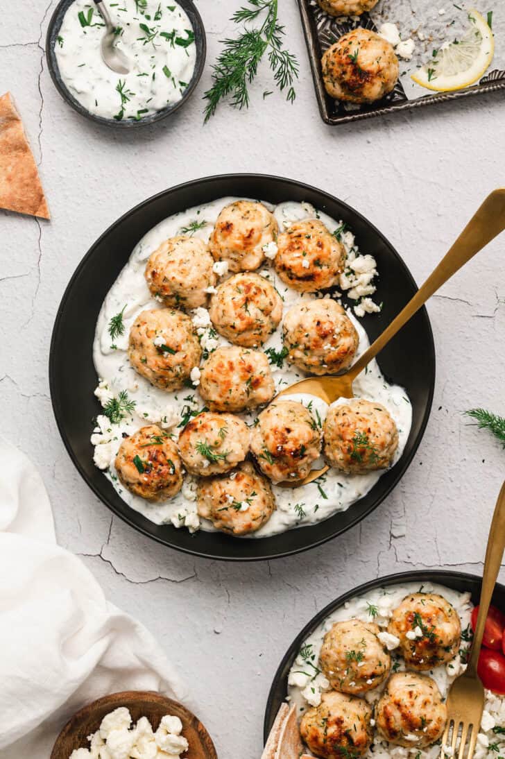 Mediterranean chicken meatballs in black bowls with yogurt sauce on the bottom.