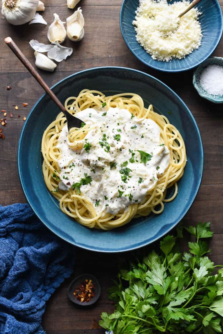 A blue bowl filled with spaghetti topped with Greek yogurt pasta sauce, chopped parsley and red pepper flakes.