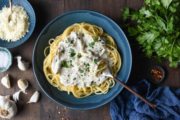 A blue bowl filled with spaghetti topped with Greek yogurt pasta sauce, chopped parsley and red pepper flakes.