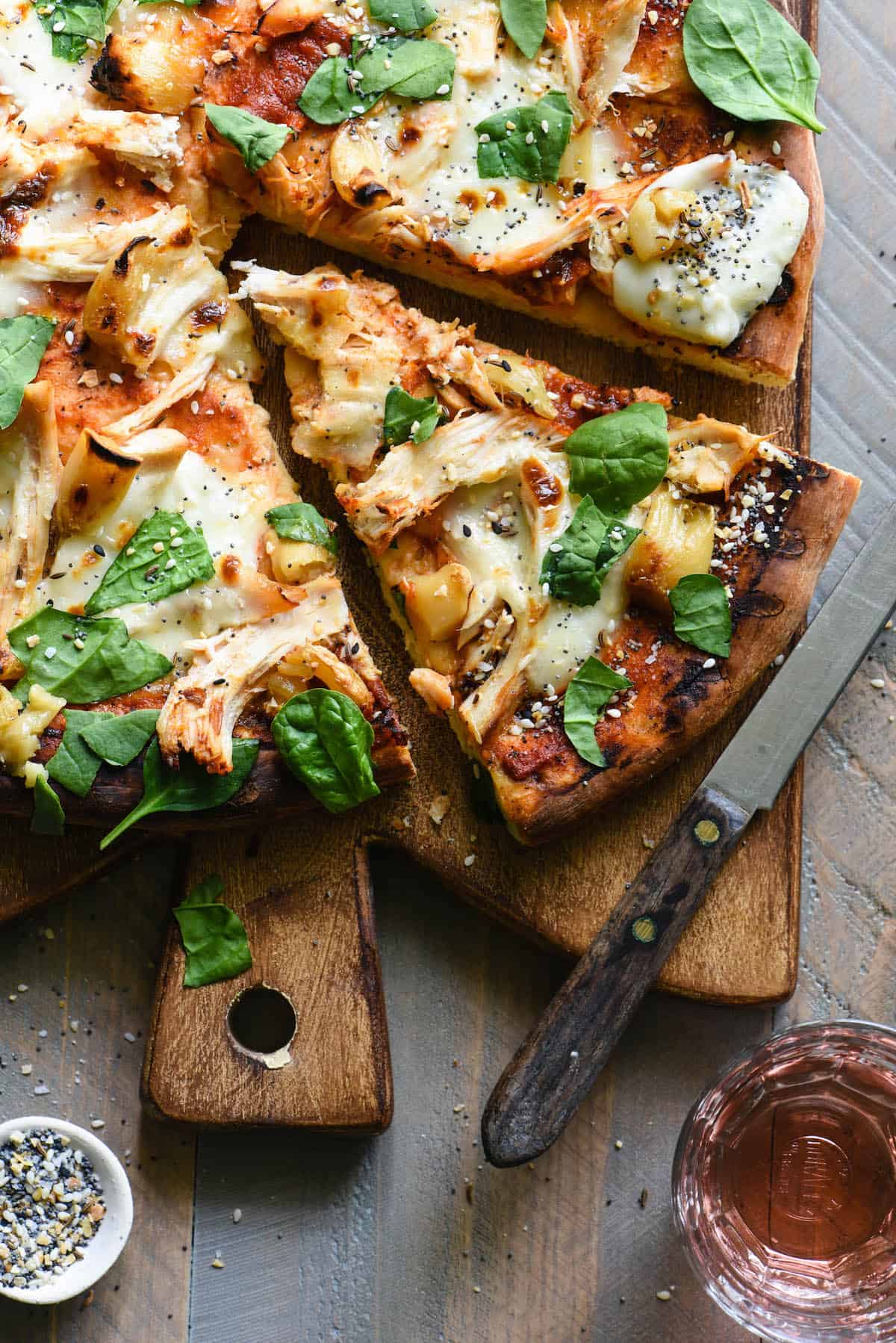 If you love homemade pizza, you have to try this Chicken Pizza with Mozzarella & Roasted Garlic! This recipe provides step-by-step instructions to either grill it like a pro, or make it in your oven. | foxeslovelemons.com Overhead photo of cut chicken pizza on cutting board with knife.