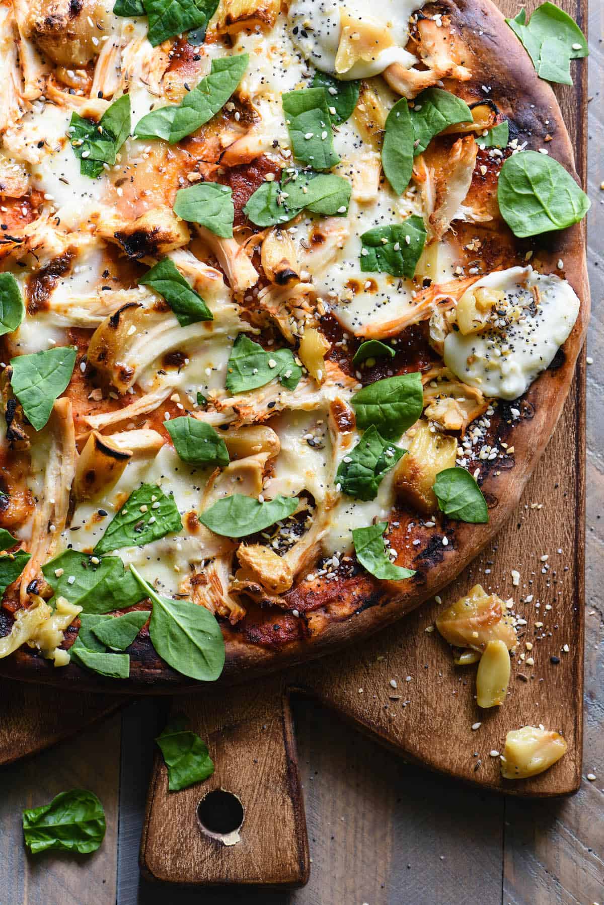 Garlic chicken pizza topped with mozzarella, chicken, roasted garlic and spinach, on wooden cutting board.