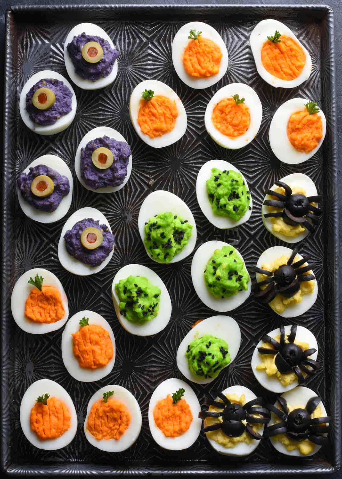 Cookie sheet with various types of Halloween deviled eggs arranged on top.