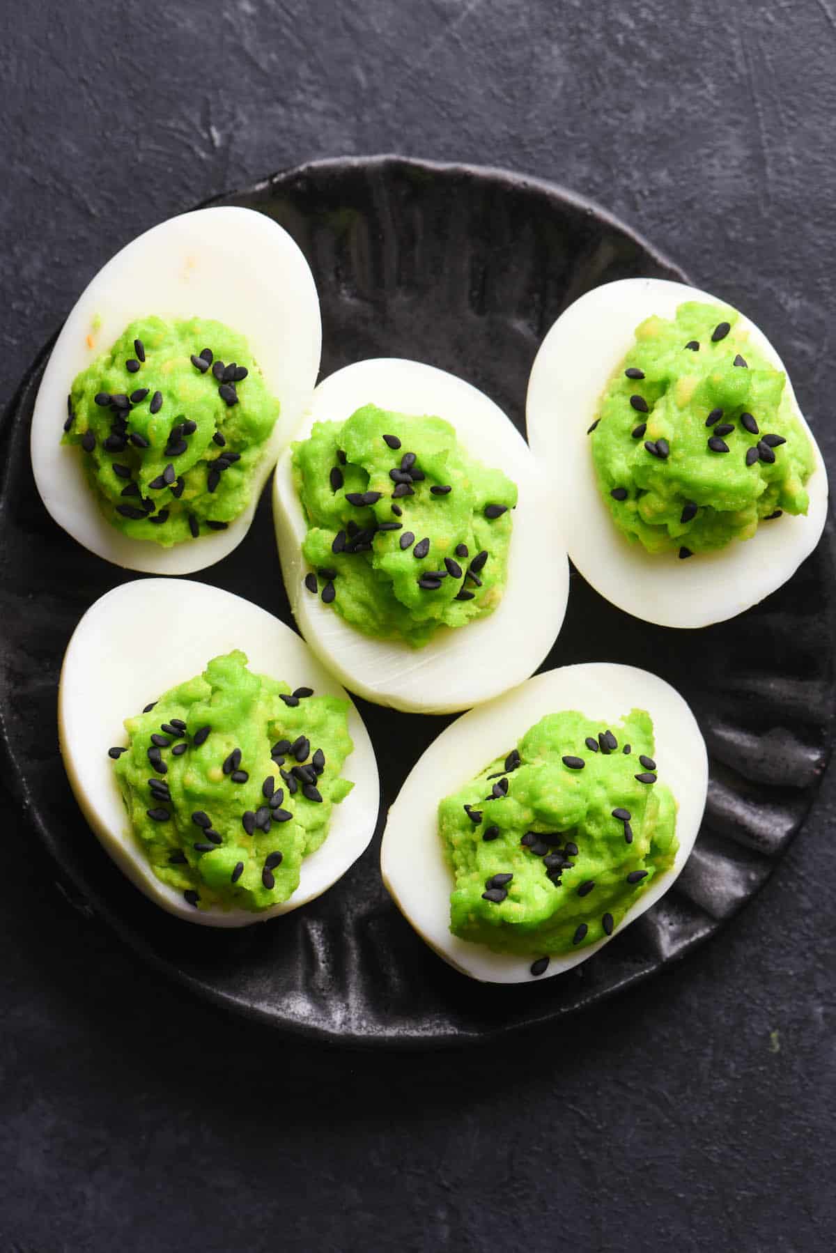 These Halloween Deviled Eggs are a spooky treat. The "trick" is that this Halloween party snack is also super easy and fast to put together! | foxeslovelemons.com Spooky deviled eggs with dyed neon green yolks, decorated with black sesame seeds.
