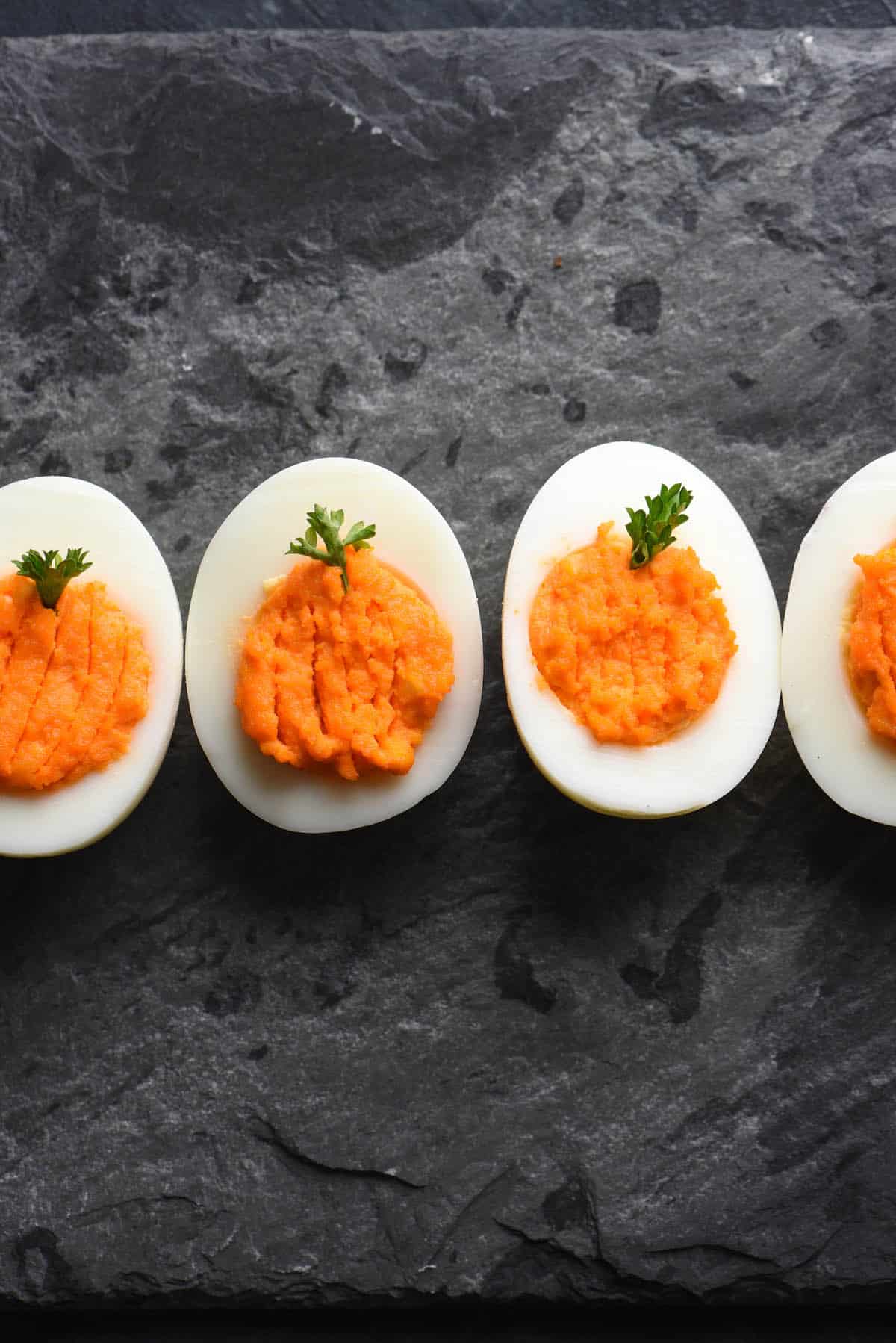 These Halloween Deviled Eggs are a spooky treat. The "trick" is that this Halloween party snack is also super easy and fast to put together! | foxeslovelemons.com Pumpkin deviled eggs with orange yolks, decorated with parsley "stems."