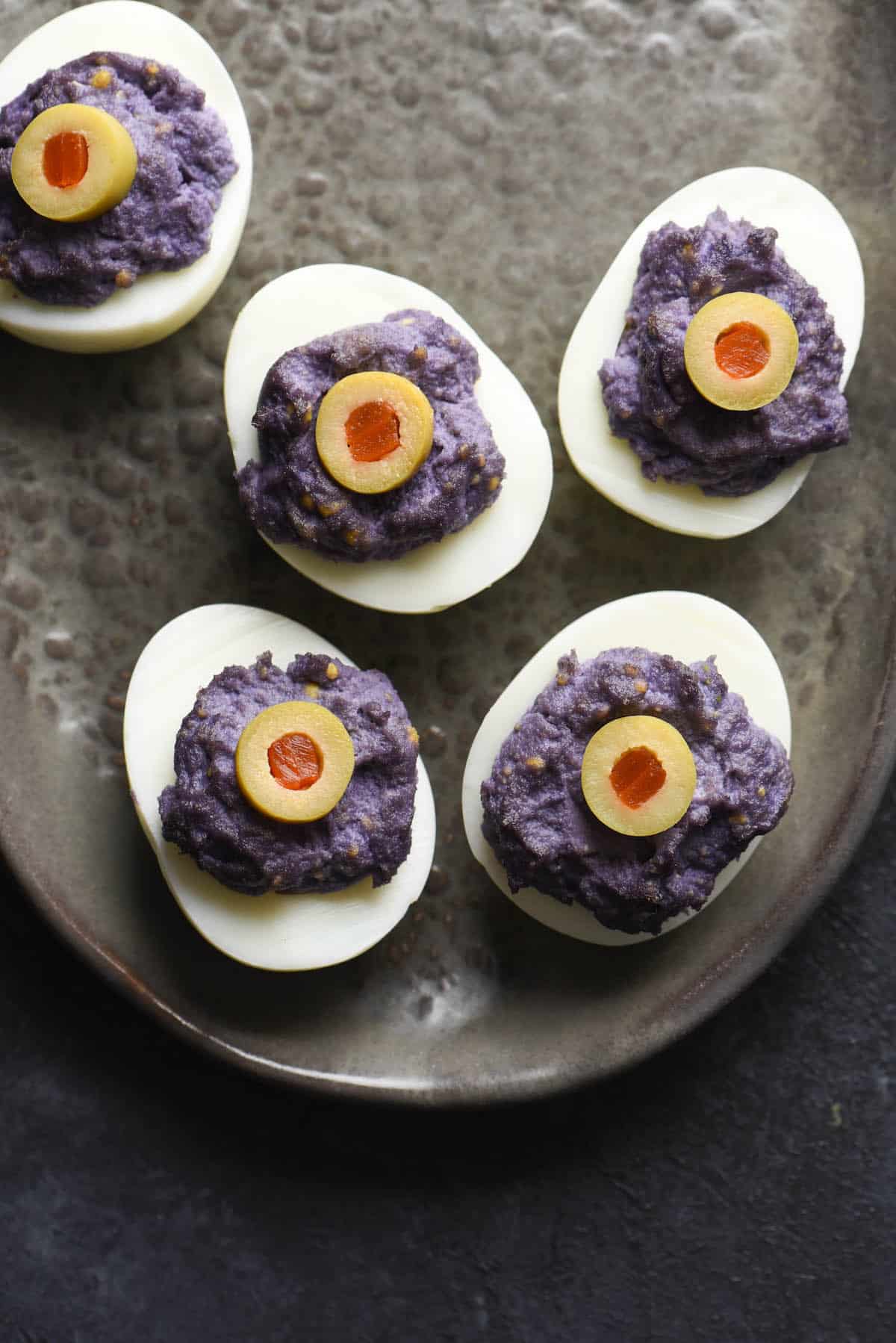 These Halloween Deviled Eggs are a spooky treat. The "trick" is that this Halloween party snack is also super easy and fast to put together! | foxeslovelemons.com Eyeball deviled eggs with dyed purple yolks and green olive "eyeballs" on top.