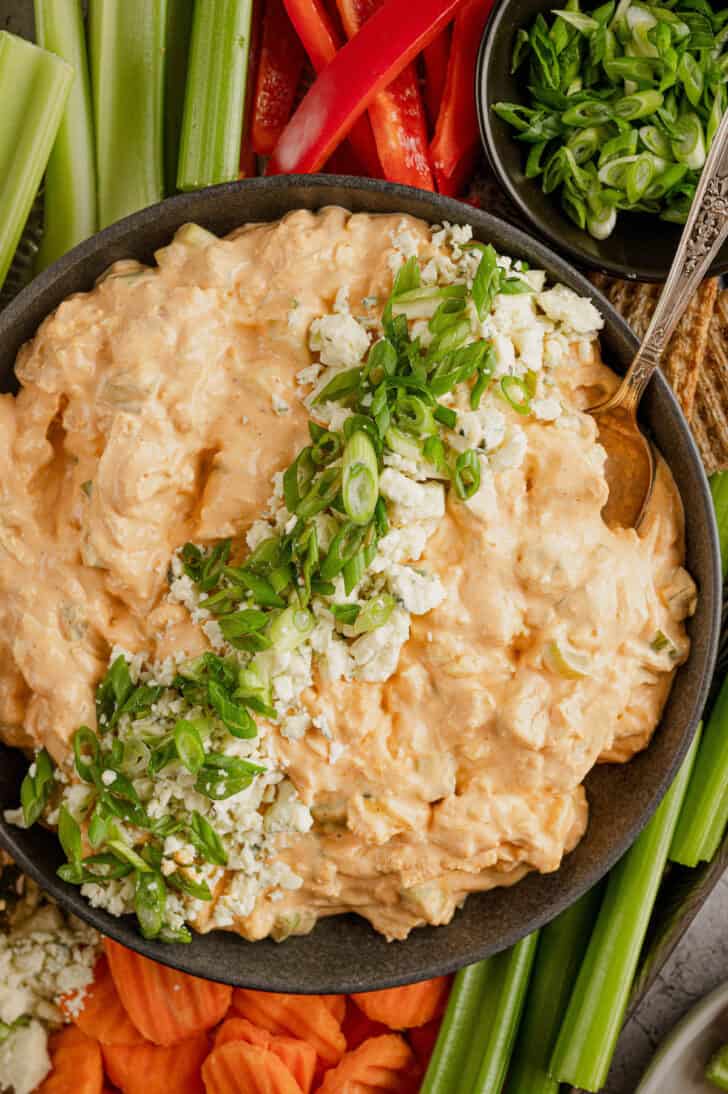 A bowl of creamy orange chicken and cheese mixture, garnished with onions and blue cheese.