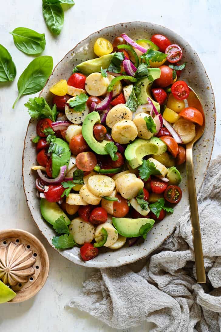 A speckled oval platter filled with hearts of palm salad made with tomatoes and avocado.
