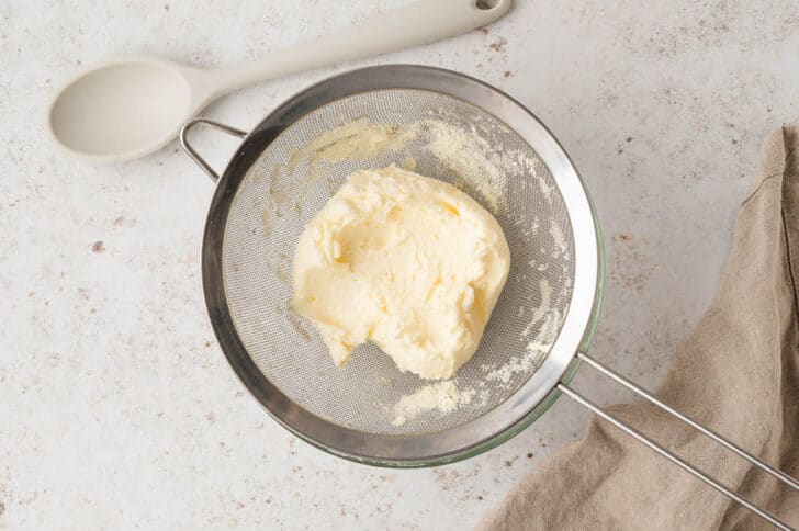 A stainless steel strainer filled with a homemade butter recipe.