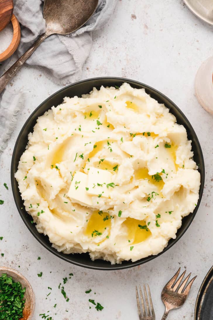 A bowl of whipped root vegetables topped with butter and parsley.