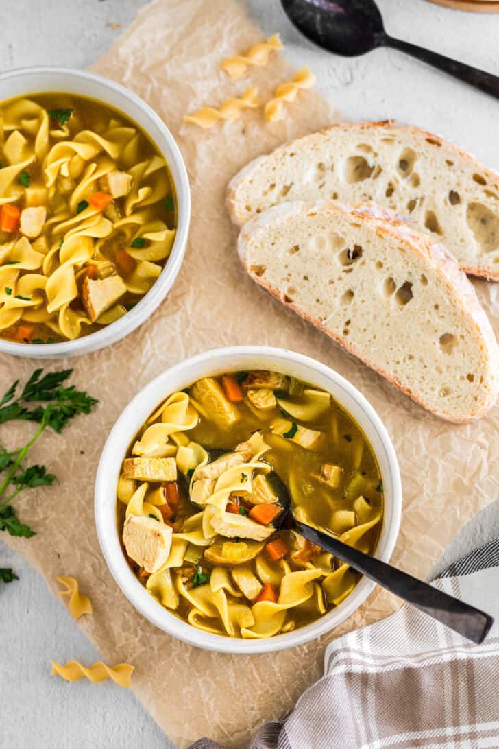 Two white bowls filled with turkey soup alongside sliced white bread.