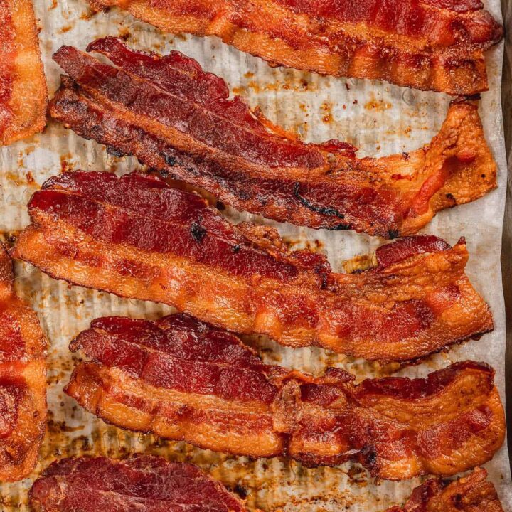 Crispy bacon lined up on a parchment paper lined baking pan.