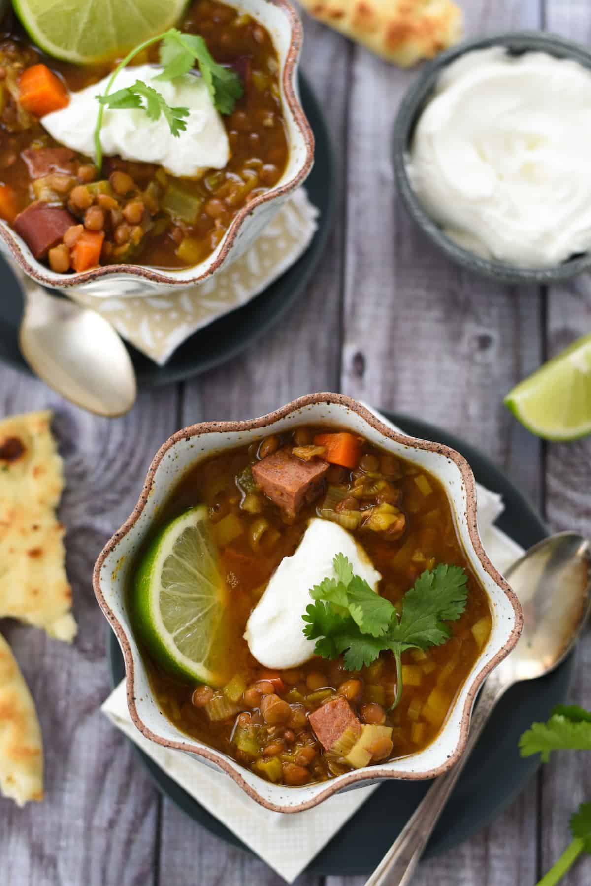This Instant Pot Lentil Soup is the absolute easiest way to get a tasty, healthy meal on the table in minutes. Put everything directly into your pressure cooker (no sautéing necessary) and cook for 15 minutes. | foxeslovelemons.com Overhead photos of two bowls of soup with lentils and sausage, with bowl of yogurt and naan bread alongside.
