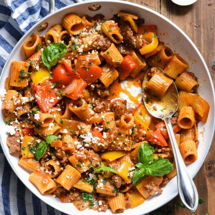 A white skillet filled with an Italian sausage pasta recipe topped with fresh herbs.