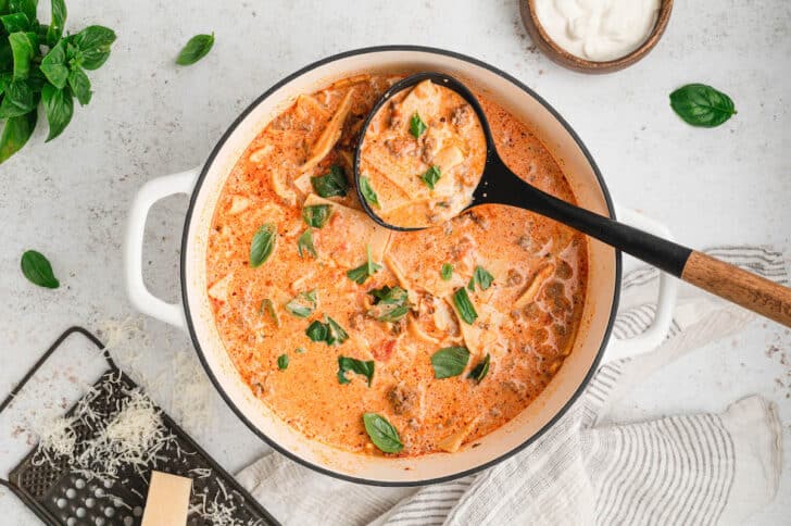 Creamy lasagna soup being ladled out of a white Dutch oven.