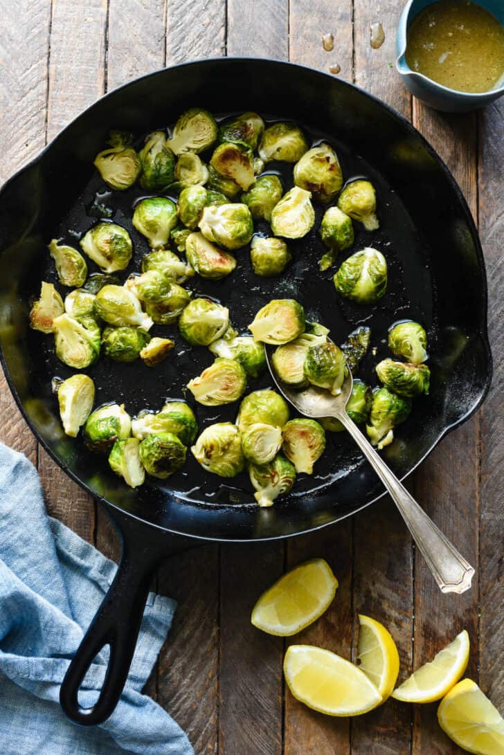 Cast iron skillet filled with baby cabbages, with lemon wedges nearby.
