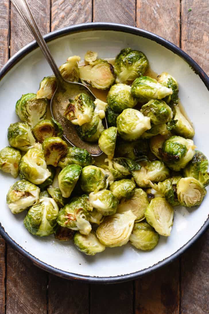 Rustic white bowl with blue rim, filled with maple glazed Brussels sprouts.
