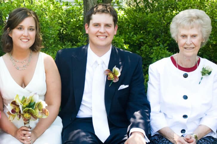 A couple of their wedding day, sitting in a row with an older woman who appears to be a grandmother.