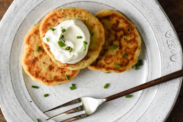 Gray plate topped with three griddled patties of spuds, garnished with sour cream and chives.