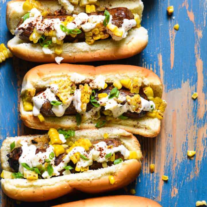 Inspired by elote, these Mexican Street Corn Brats are ideal for a summer celebration or easy weeknight meal! Spicy sausages are topped with fresh sweet corn, creamy lime sauce and tangy cheese. | foxeslovelemons.com