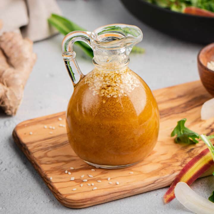 Miso ginger dressing in a small glass carafe, with a fresh vegetable salad in the background.