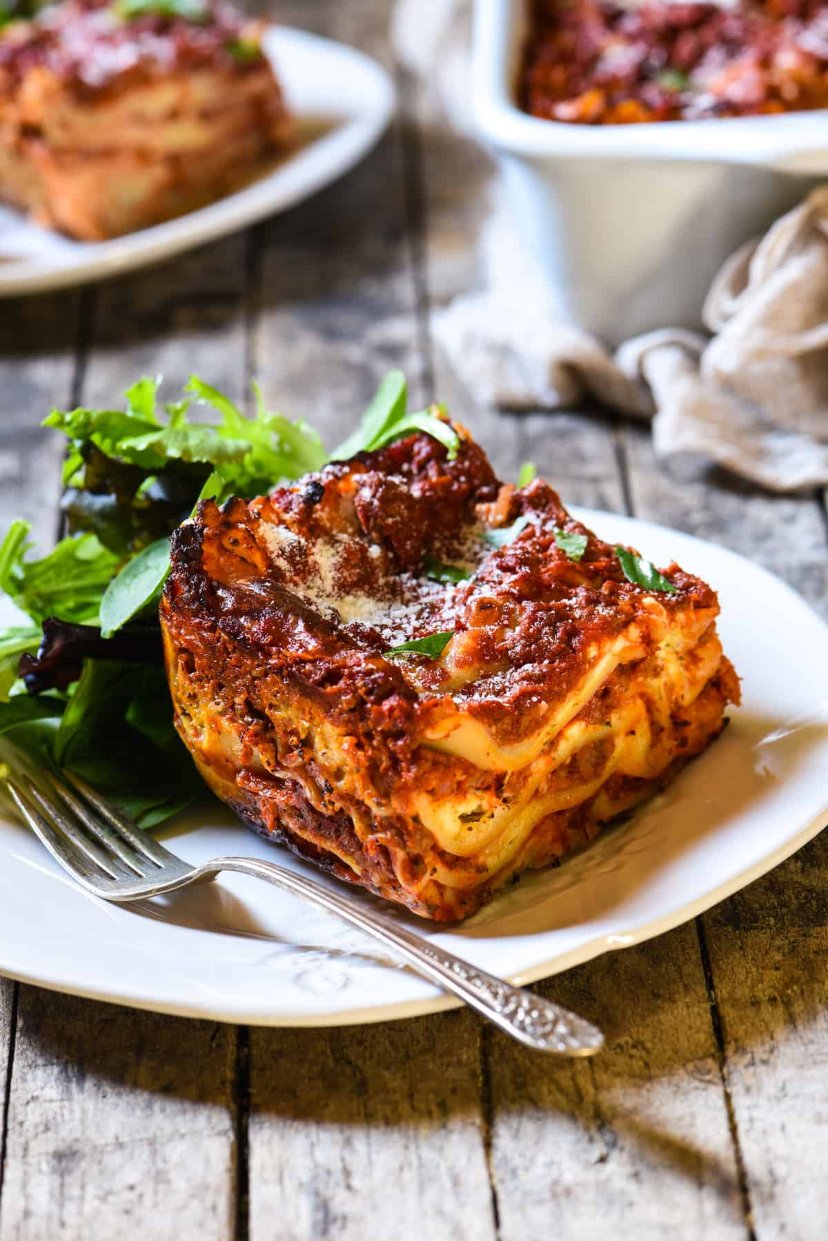 Lasagna with Cottage Cheese - A classic Midwestern noodle casserole. Layers of rich meat sauce, pasta, creamy filling and cheese will have the whole family coming back for seconds! | foxeslovelemons.com Piece of lasagna recipe with cottage cheese with a side salad on a rustic white plate.