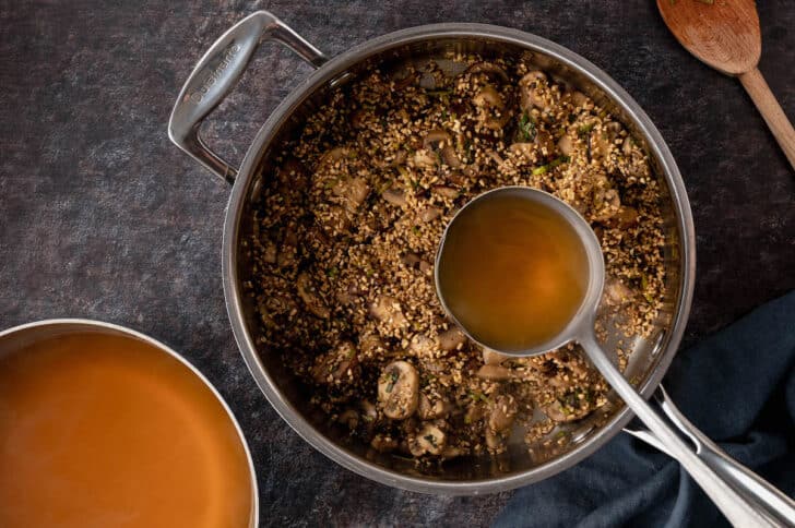 Ladle pouring stock into a skillet of savory steel cut oats.