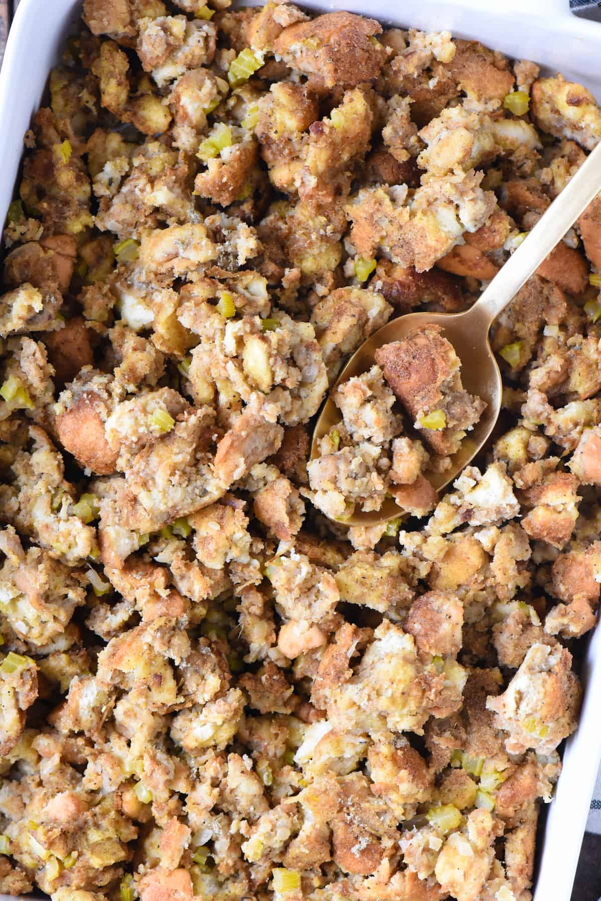 A recipe for Grandma's Old Fashioned Bread Stuffing, a classic and old fashioned Thanksgiving bread dressing made with milk, turkey stock, onions, celery and herbs. | foxeslovelemons.com Closeup of baking dish of old fashioned bread stuffing with serving spoon.