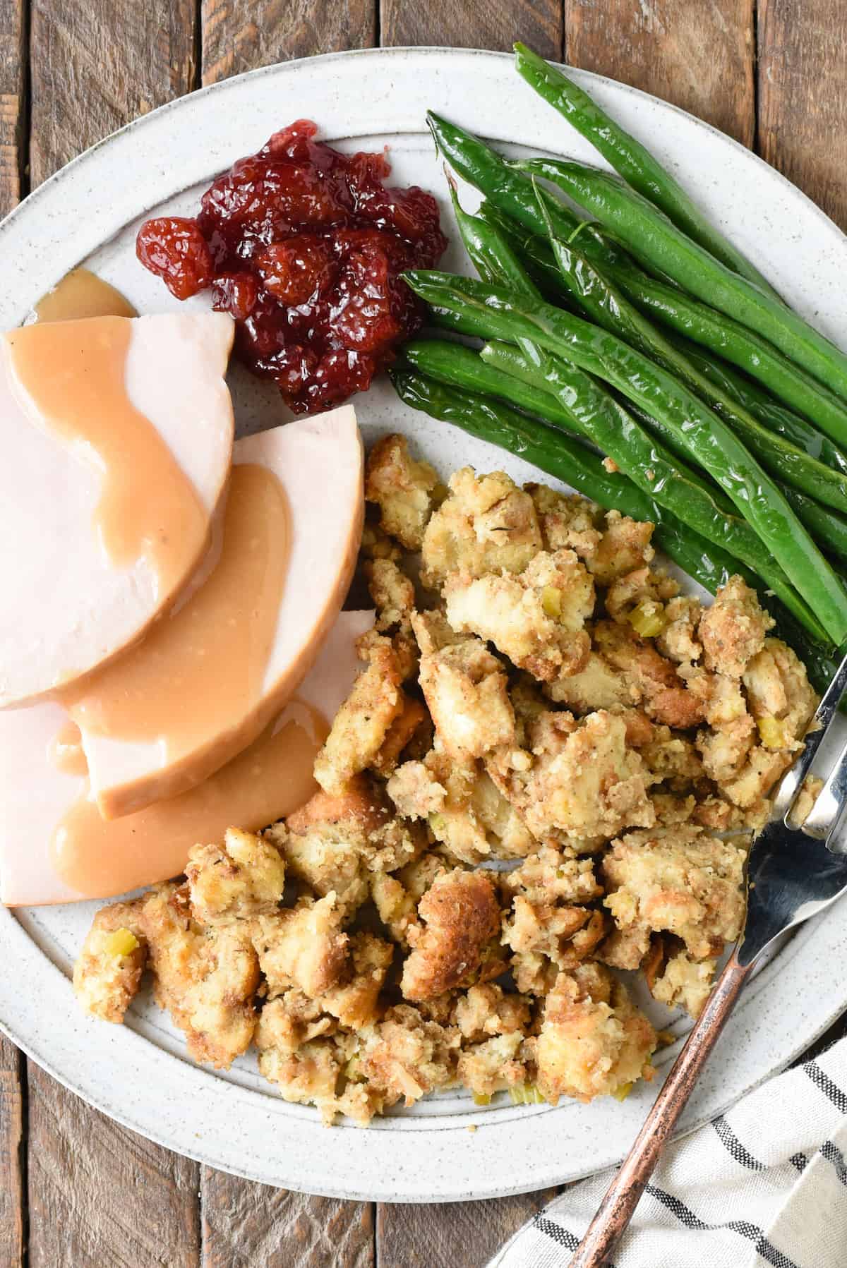 A recipe for Grandma's Old Fashioned Bread Stuffing, a classic and old fashioned Thanksgiving bread dressing made with milk, turkey stock, onions, celery and herbs. | foxeslovelemons.com Plate of Thanksgiving dinner, with turkey and gravy, bread stuffing, cranberry sauce and green beans.