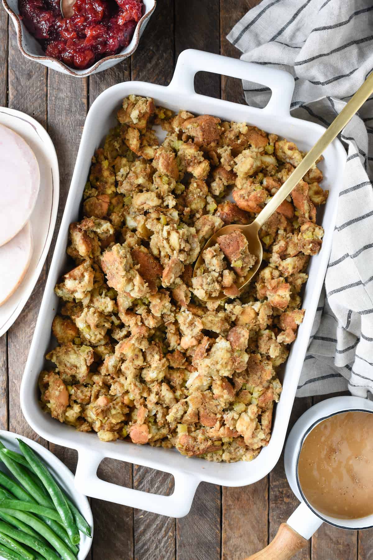 A recipe for Grandma's Old Fashioned Bread Stuffing, a classic and old fashioned Thanksgiving bread dressing made with milk, turkey stock, onions, celery and herbs. | foxeslovelemons.com Overhead Thanksgiving tablescape with stuffing, turkey, cranberry sauce, green beans and gravy.
