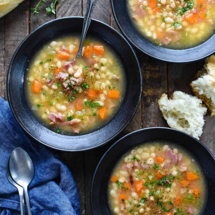 Three black bowls filled with old fashioned ham and bean soup on a rustic wooden tabletop.