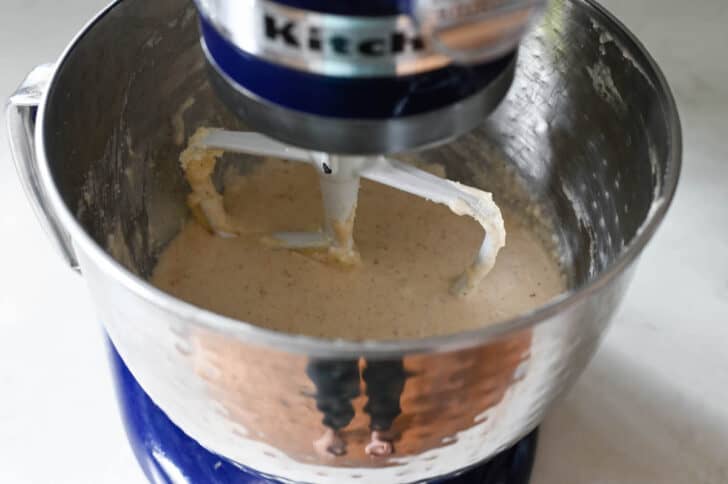 A light brown batter mixture in a Kitchenaid stand mixer bowl being beat with the paddle attachment.