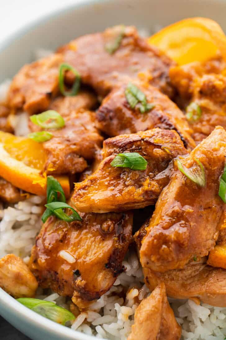 Closeup on ginger and orange chicken garnished with green onions, over white rice.