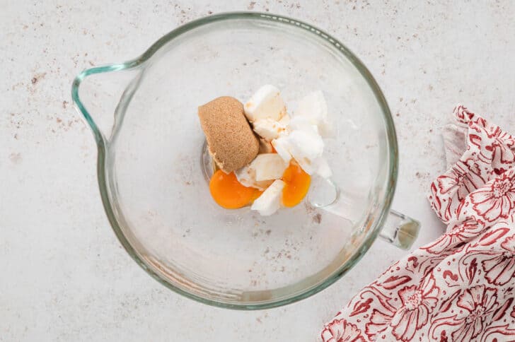 A glass stand mixer bowl with eggs, brown sugar and shortening in it.