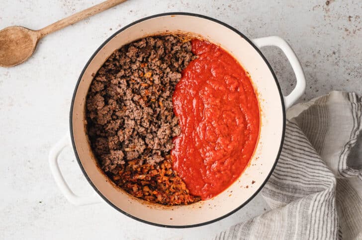 Cooked ground beef and marinara sauce in a white Dutch oven.