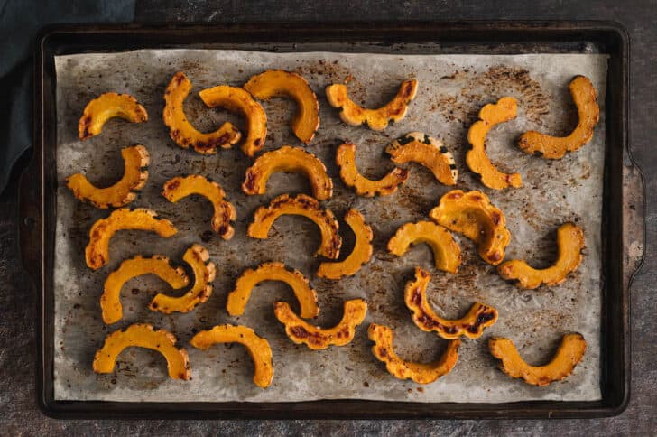 A baking pan topped with roasted half moon slices of a fall gourd.