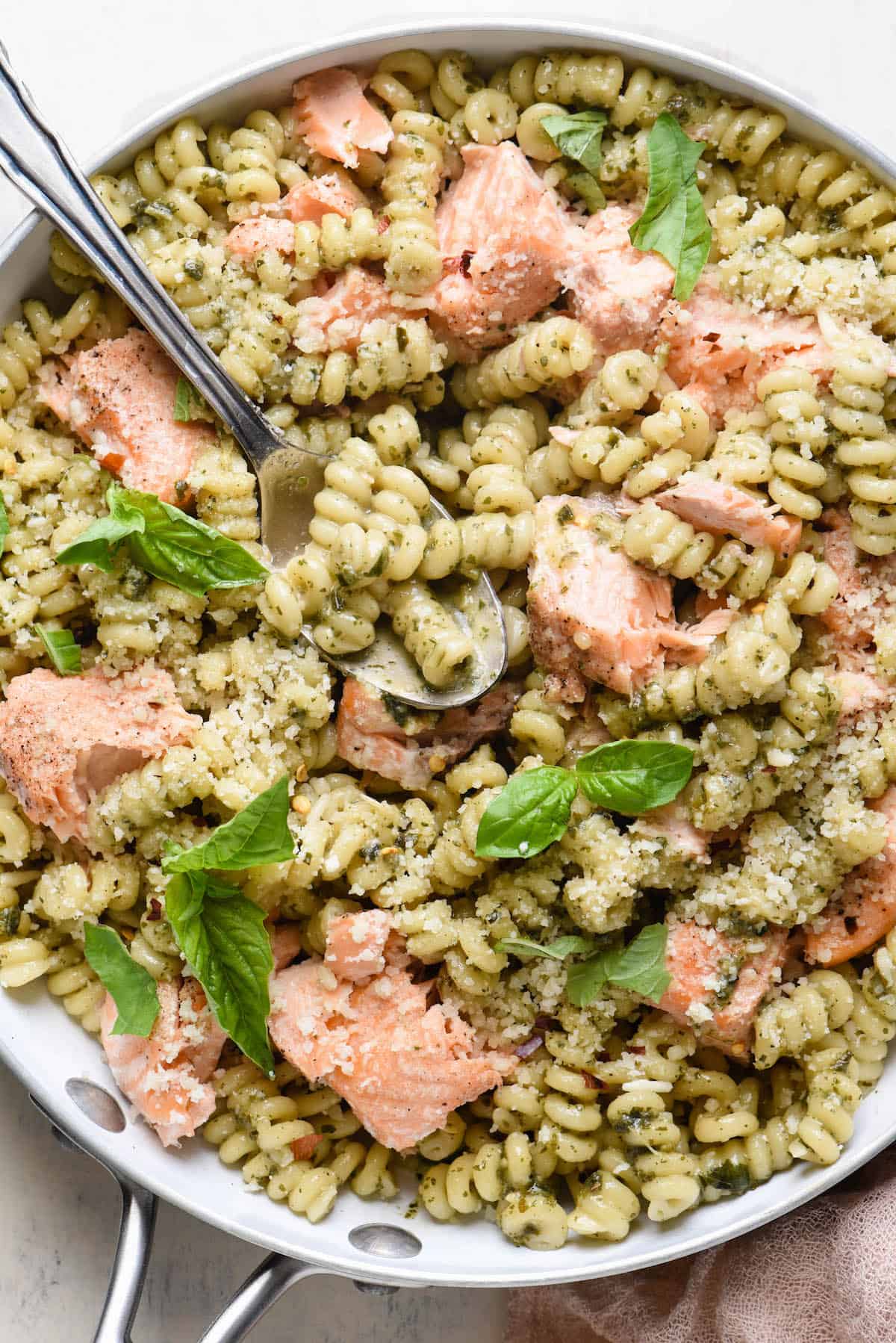 This Salmon Pesto Pasta is a restaurant quality dish that you can make at home. So flavorful, and easy enough to make on a weeknight! | foxeslovelemons.com Closeup photo of salmon pasta with pesto, in white skillet.