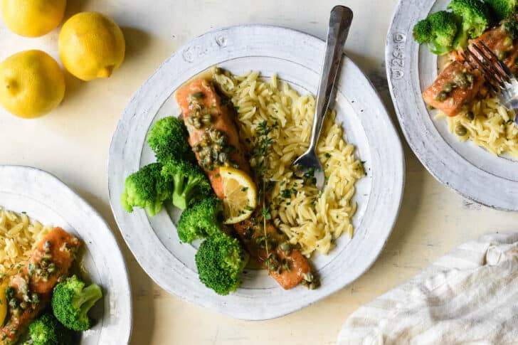 Fish with lemon caper sauce, served on a rustic plate with orzo and steamed broccoli.