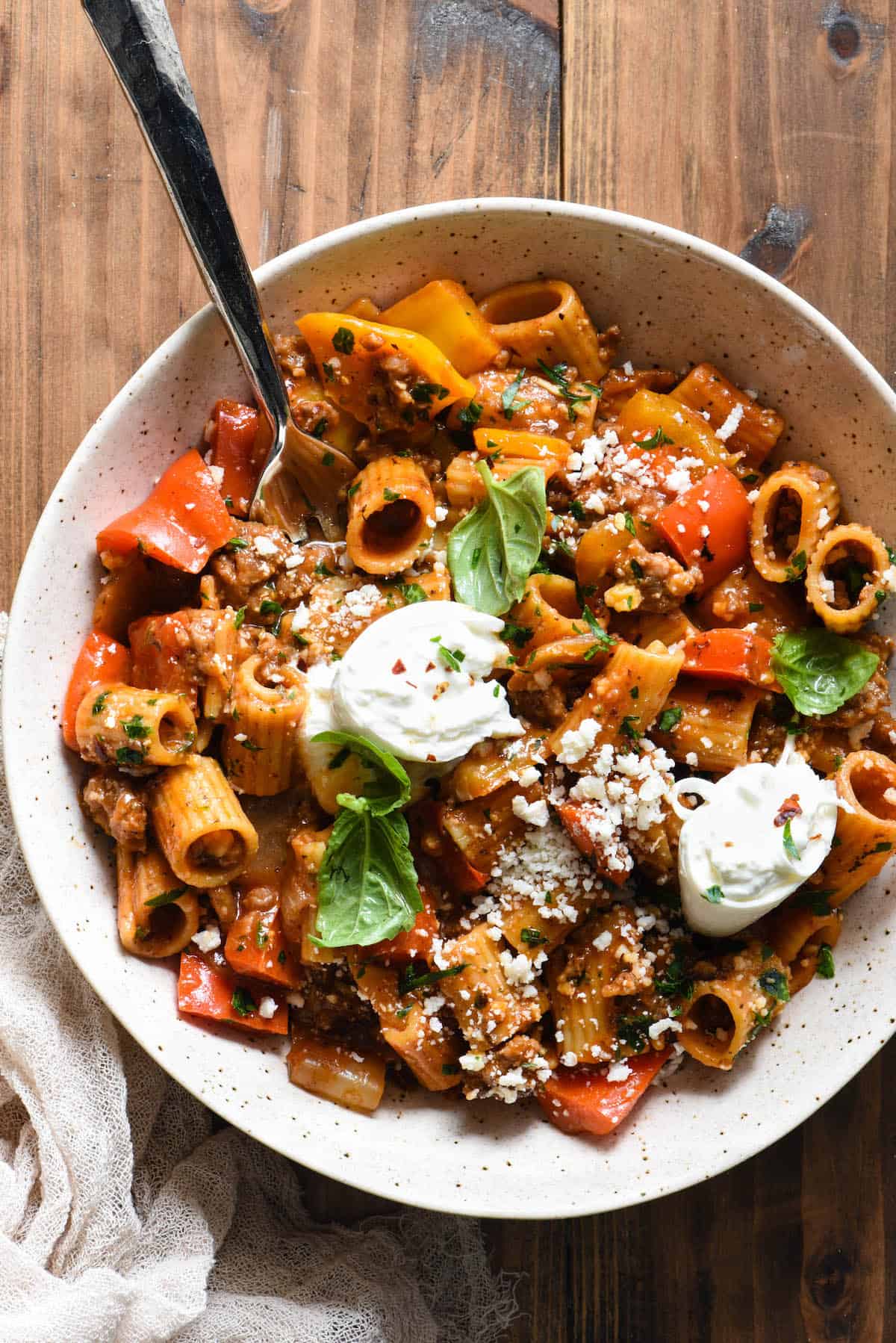 This Italian Sausage Pasta Skillet Dinner is a comforting yet veggie-packed meal that is made from start to finish in JUST ONE SKILLET. | foxeslovelemons.com A speckled bowl filled with sausage and peppers pasta topped with fresh herbs and chunks of burrata cheese.