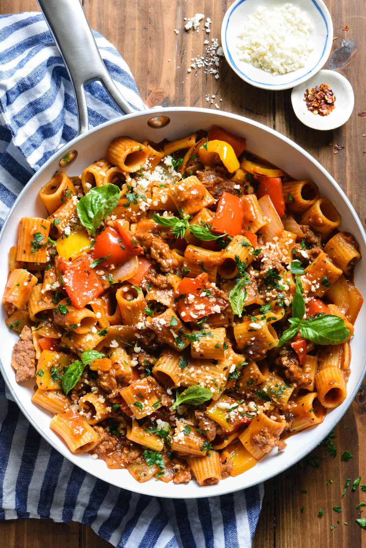 This Italian Sausage Pasta Skillet Dinner is a comforting yet veggie-packed meal that is made from start to finish in JUST ONE SKILLET. | foxeslovelemons.com A white skillet filled with pasta with sausage and peppers topped with fresh herbs.