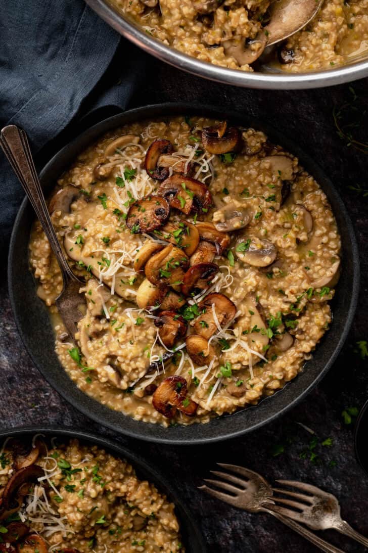 A dark shallow bowl filled with savory oatmeal topped with mushrooms, herbs and Parmesan cheese.
