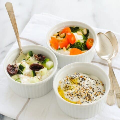 Three white ramekins of Greek yogurt topped with savory toppings.
