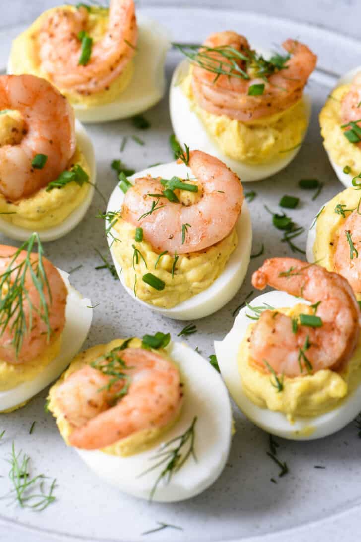 Shrimp deviled eggs garnished with chives and dill on a light gray plate.