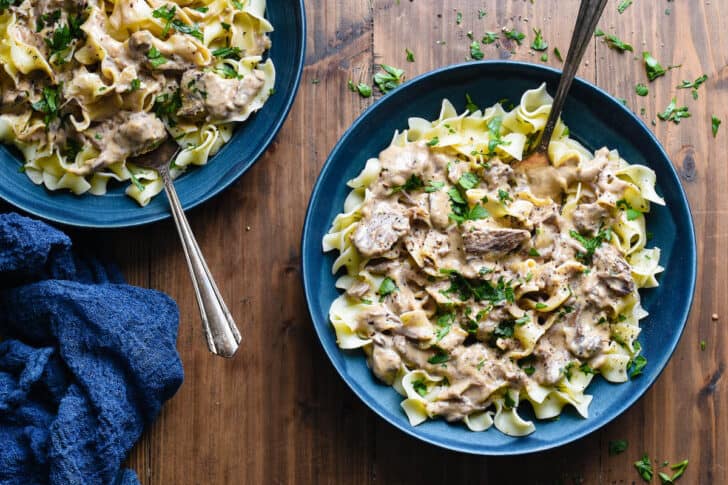 Two blue bowls filled with beef stroganoff crock pot on a wooden background with a blue napkin.