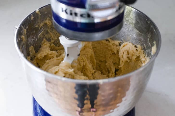 A light brown batter mixture in a Kitchenaid stand mixer bowl being beat with the paddle attachment.