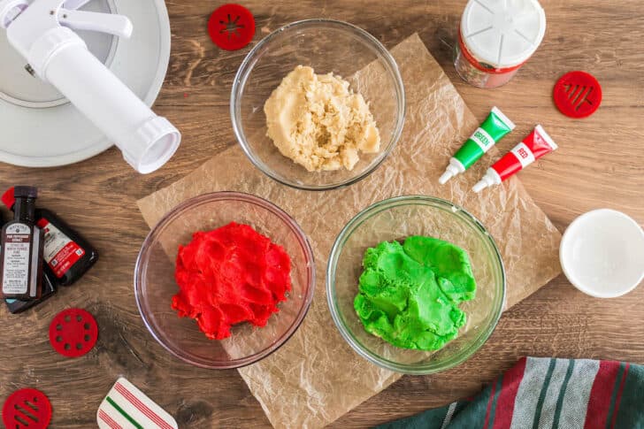 Three glass bowls filled with dough for dyed red, green and un-dyed.