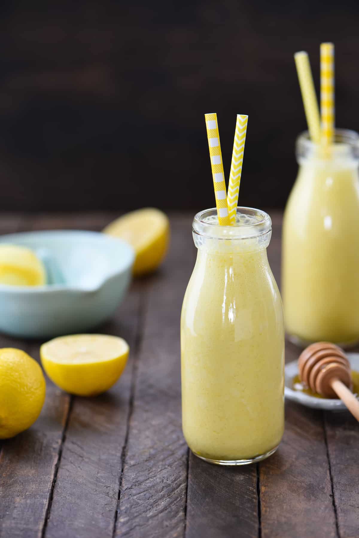 This Lemon Smoothie is like sunshine in a bottle! Yogurt, lemon, honey, ginger and turmeric will wake you up on a sleepy morning. | foxeslovelemons.com Two small glass bottles filled with lemon smoothie, with yellow straws sticking out of the bottles.